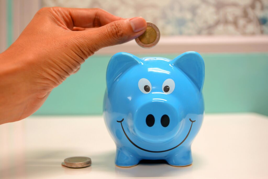 pexels-photo-1602726-1602726 Hand inserting a coin into a blue piggy bank for savings and money management.